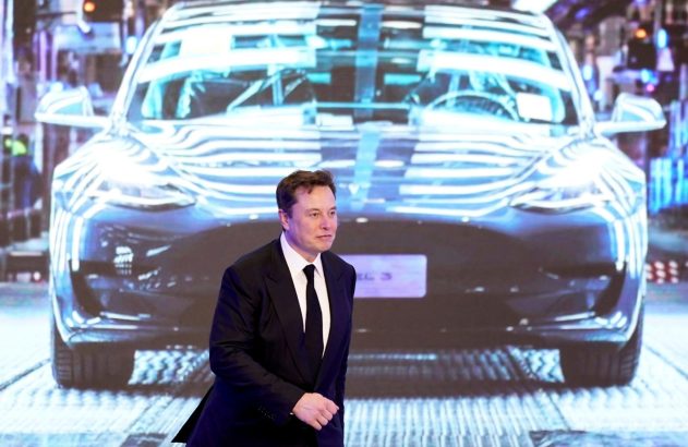Elon Musk de terno caminha à frente de projeção digital de um carro Tesla em um evento.