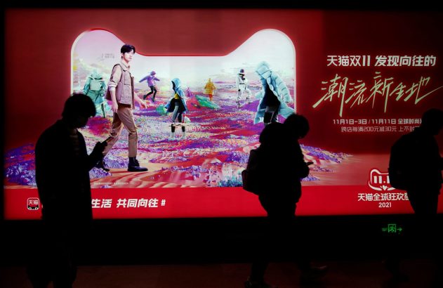 Silhuetas passam por vibrante outdoor da Tmall 11.11 com moda futurista e celebridade.