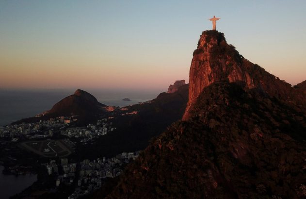 Vista panorâmica do Cristo Redentor no Corcovado, Rio de Janeiro, ao pôr do sol, com cidade, montanhas e mar.