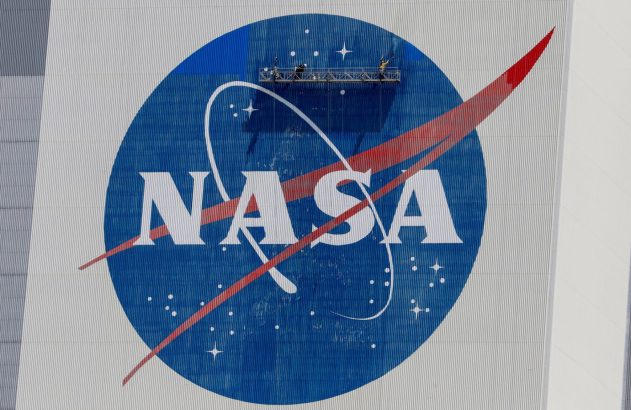 Pessoas em andaime pintam o logotipo da NASA em um prédio corrugado.