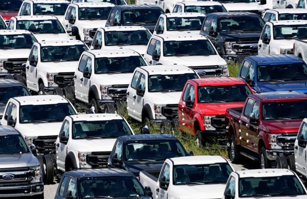 Pátio com diversos caminhões Ford novos, a maioria brancos. Muitos são modelos chassi-cabine, aguardando finalização.