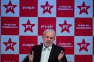 Homem de terno e barba gesticula em frente a painel xadrez do Partido dos Trabalhadores (PT).