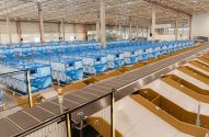 Armazém de logística com longas esteiras transportadoras e filas de caixas de triagem azuis em um sistema automatizado.