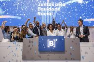 Grupo diverso celebra na B3 com confetes azuis, em frente a tela "Juntos pela Equidade Racial".