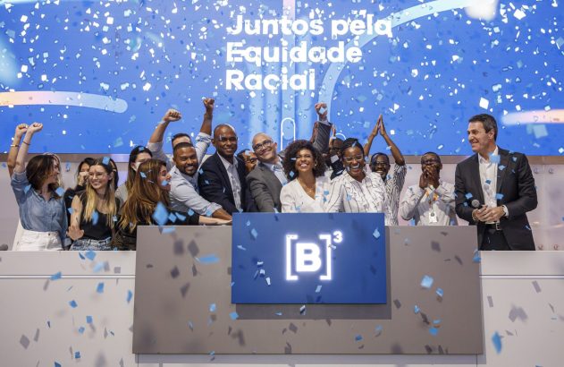 Grupo diverso celebra na B3 com confetes azuis, em frente a tela "Juntos pela Equidade Racial".