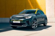 Carro Kia Stonic cinza com teto amarelo, estacionado em frente a uma parede colorida.
