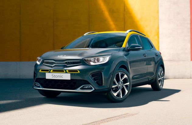 Carro Kia Stonic cinza com teto amarelo, estacionado em frente a uma parede colorida.