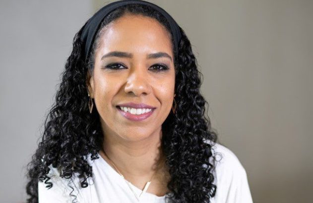 Retrato de mulher sorrindo com cabelo cacheado preto e faixa na cabeça.