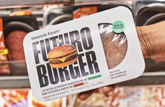 Mão segura embalagem de Futuro Burger, hambúrguer à base de plantas, em prateleira de mercado.