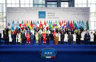 Foto de grupo de líderes mundiais e autoridades em cúpula do G20, com bandeiras e logo G20 ao fundo.