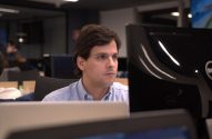 Homem de camisa azul focado em uma tela de computador no escritório.