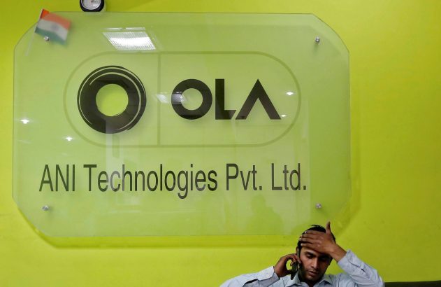 Placa de vidro da OLA/ANI Technologies em parede verde-limão, homem fala ao telefone com a mão na cabeça.