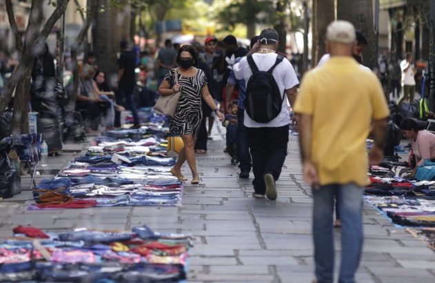 Mercado de rua movimentado: pessoas caminhando e roupas à venda no chão.