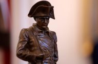 Estátua de bronze de Napoleão Bonaparte com seu chapéu bicorne e casaco militar, olhando para baixo.