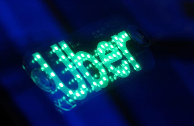Sinal Uber com LEDs verdes, sobre fundo escuro.