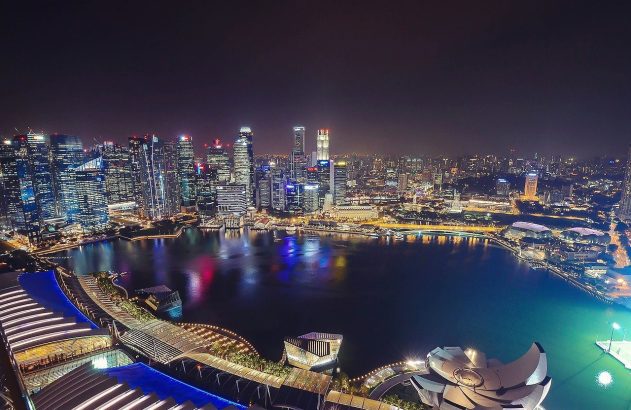 Panorama noturno da Baía de Marina em Singapura, com arranha-céus iluminados e reflexos na água.