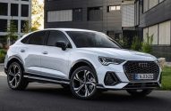 Carro Audi branco, estilo SUV cupê, estacionado em rua com prédios modernos ao fundo.