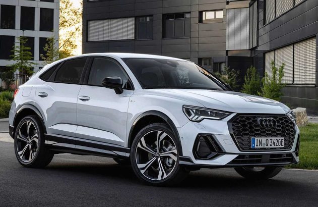 Carro Audi branco, estilo SUV cupê, estacionado em rua com prédios modernos ao fundo.