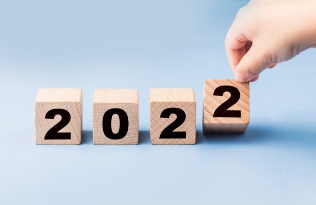 Mão posicionando bloco de madeira com o número '2' para formar '2022'.