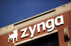 Letreiro branco da Zynga com logo de cachorro em prédio de tijolos vermelhos sob céu azul.