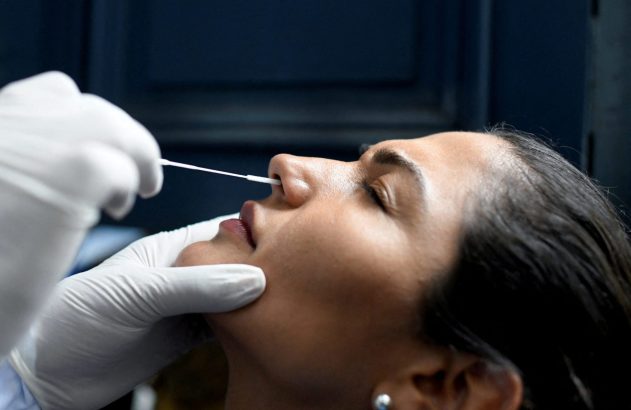 Uma mulher faz teste de swab nasal, com uma mão enluvada inserindo o cotonete em seu nariz.