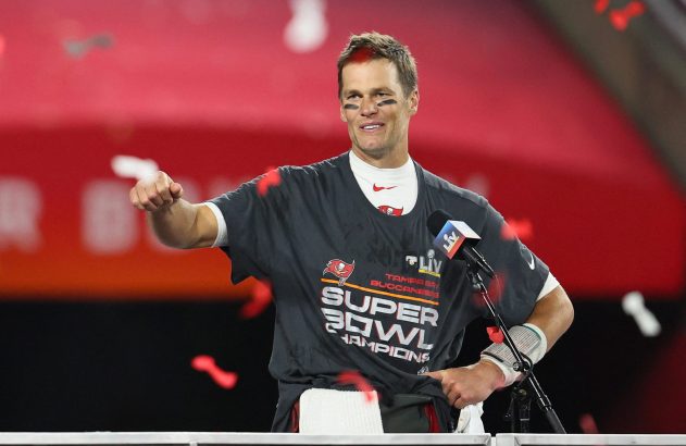 Tom Brady sorrindo, camisa de campeão, punho cerrado, confete vermelho caindo em celebração do Super Bowl.