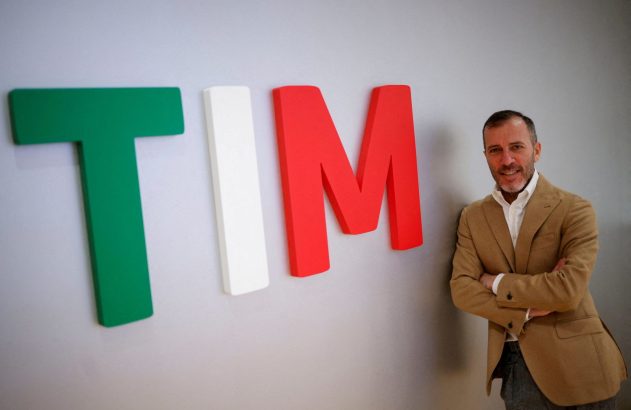 Homem sorrindo, braços cruzados, ao lado do logo TIM com letras verde, branco e vermelho (cores da Itália).