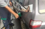 Frentista abastece carro cinza adesivado em posto de combustível.