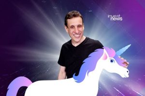 Homem sorrindo de camiseta preta, ao lado de um unicórnio branco com crina colorida. Fundo abstrato com brilho.