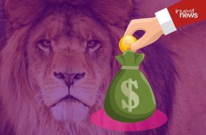Mão depositando moeda em saco de dinheiro com cifrão, em fundo roxo com um leão.