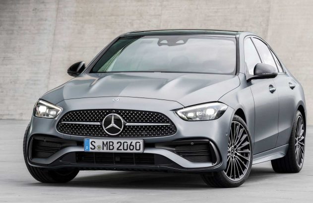 Mercedes-Benz C-Class cinza, visão frontal-esquerda. Carro estacionado com grade e faróis acesos.