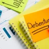 Papéis com gráficos e um post-it escrito debêntures, com canetas marca-texto ao lado
