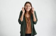 Mulher de olhos fechados e feição contraída, fazendo um pedido com os dedos cruzados.