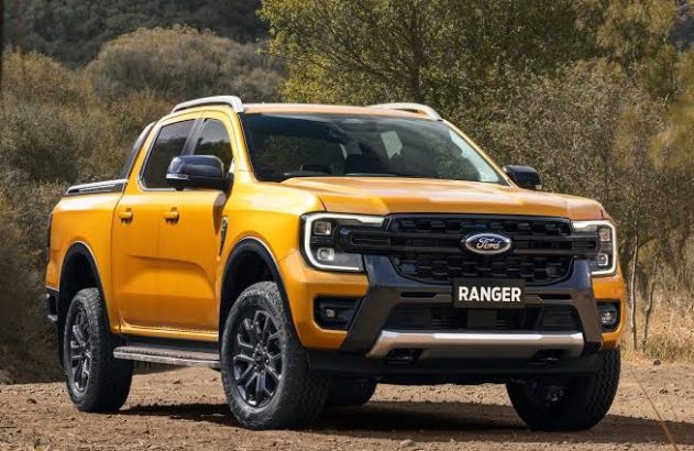 Picape Ford Ranger amarela em estrada de terra, com vegetação ao fundo.