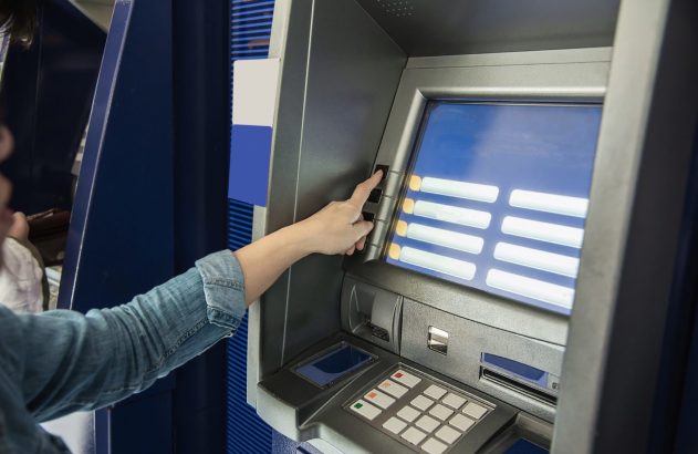Mão de pessoa apertando botão ao lado da tela de um caixa eletrônico.