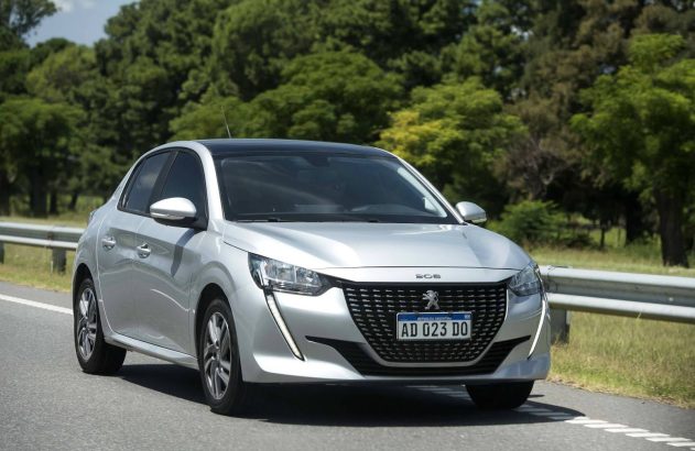 Um Peugeot 208 prata em movimento numa estrada com fundo verde e guarda-corpo.