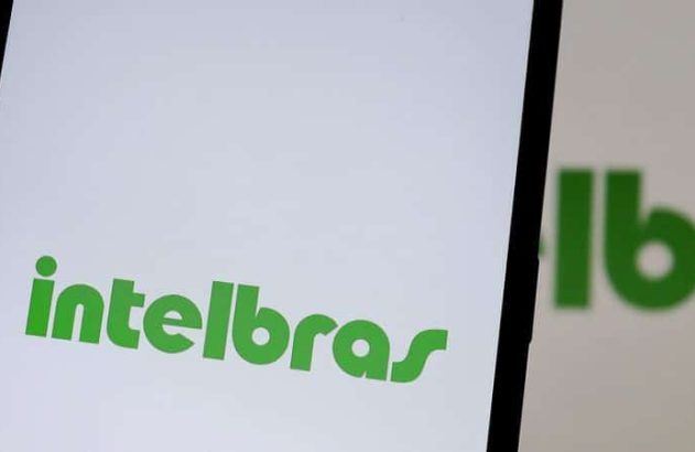 Close-up de smartphone exibindo logo 'Intelbras' verde na tela branca. Reflexo e mão segurando aparelho.