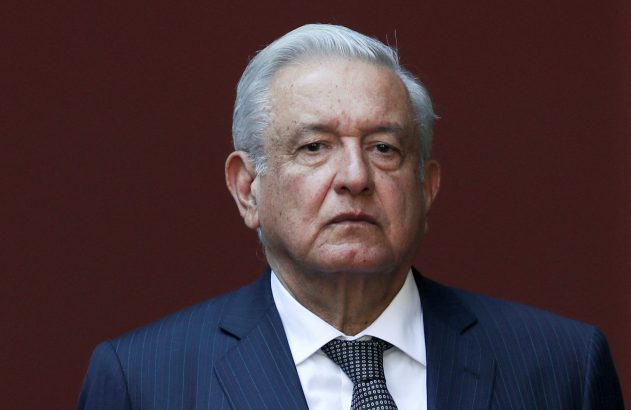 Retrato de homem com cabelos grisalhos, terno listrado e gravata. Olha para frente. Fundo marrom escuro.