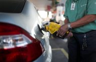 Frentista abastece carro cinza em posto de gasolina com bico amarelo.