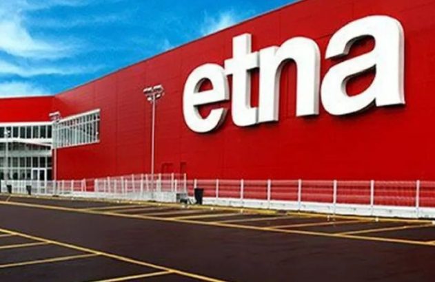 Prédio vermelho com letreiro branco 'etna' e estacionamento vazio em frente.