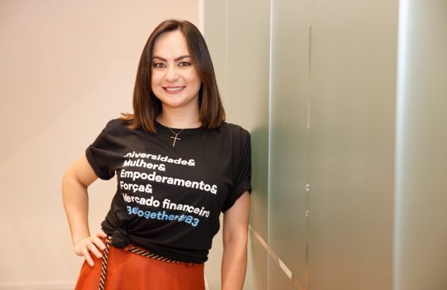 Mulher sorridente com camiseta preta estampada e saia laranja, posando em ambiente interno.