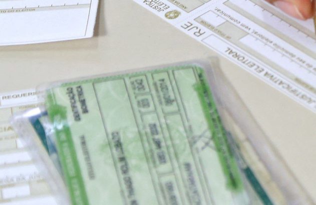 Pessoa preenchendo formulário de justificativa eleitoral com caneta, próximo a documentos eleitorais.