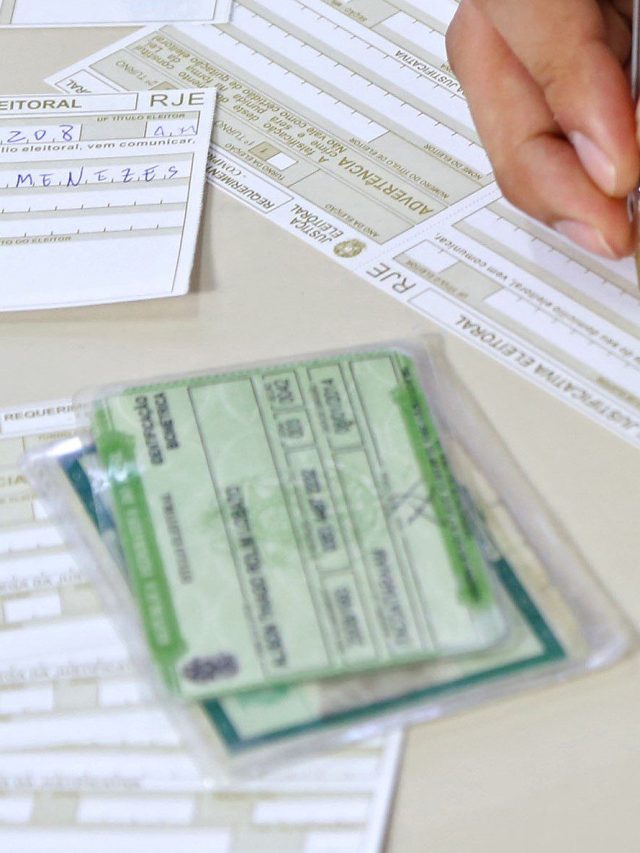 Pessoa preenchendo formulário de justificativa eleitoral com caneta, próximo a documentos eleitorais.