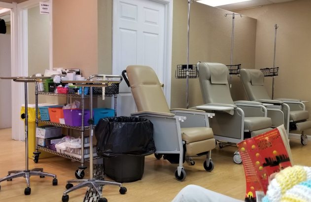 Sala de infusão com poltronas e postes de soro. Suprimentos médicos e pessoa lendo um livro.