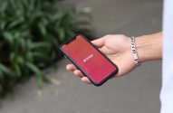 Mão segura smartphone exibindo o logo e nome do app Tinder em tela cheia. Pulso com pulseira.