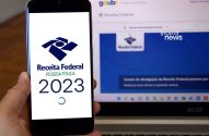 Pessoa com celular e notebook exibindo o app e site da Receita Federal (Imposto de Renda 2023).