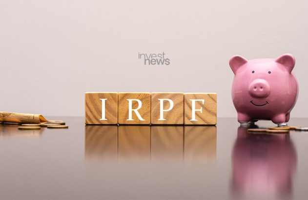 Blocos de madeira com IRPF, um cofrinho rosa e moedas com nota. Representa imposto de renda e poupança.