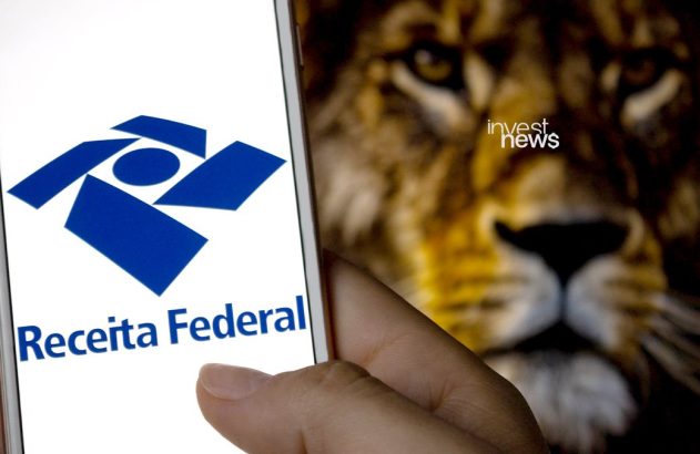 Mão segura smartphone com logo da Receita Federal. Fundo desfocado mostra rosto de leão.
