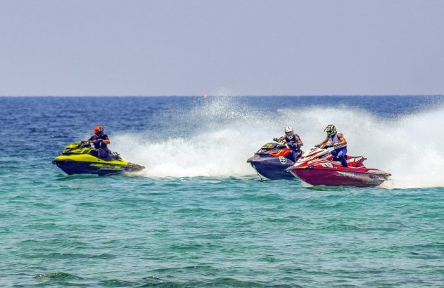Três jet skis com pilotos na água, gerando grande spray ao acelerar.