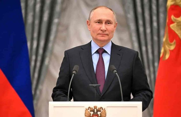 Vladimir Putin de terno e gravata, discursando em pódio com bandeiras russas ao fundo.